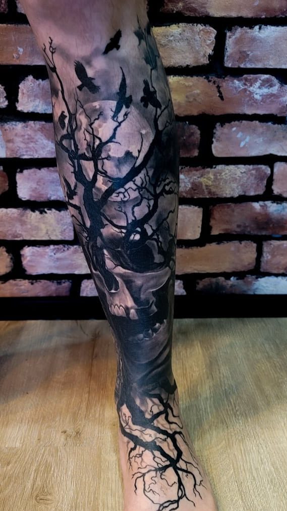 Forest silhouette with birds and a skull, blackwork tattoo on a lower leg